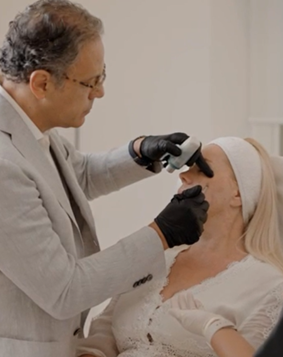 Dr. Dany Touma injecting fillers into a female patient's face at a cosmetic clinic