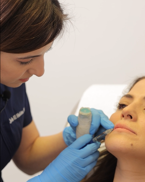 Dr. Joelle El Hakim injecting fillers into a female patient's lips at a cosmetic clinic